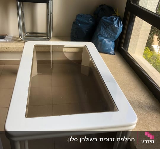 שולחן עם משטח זכוכית שקוף במסגרת לבנה